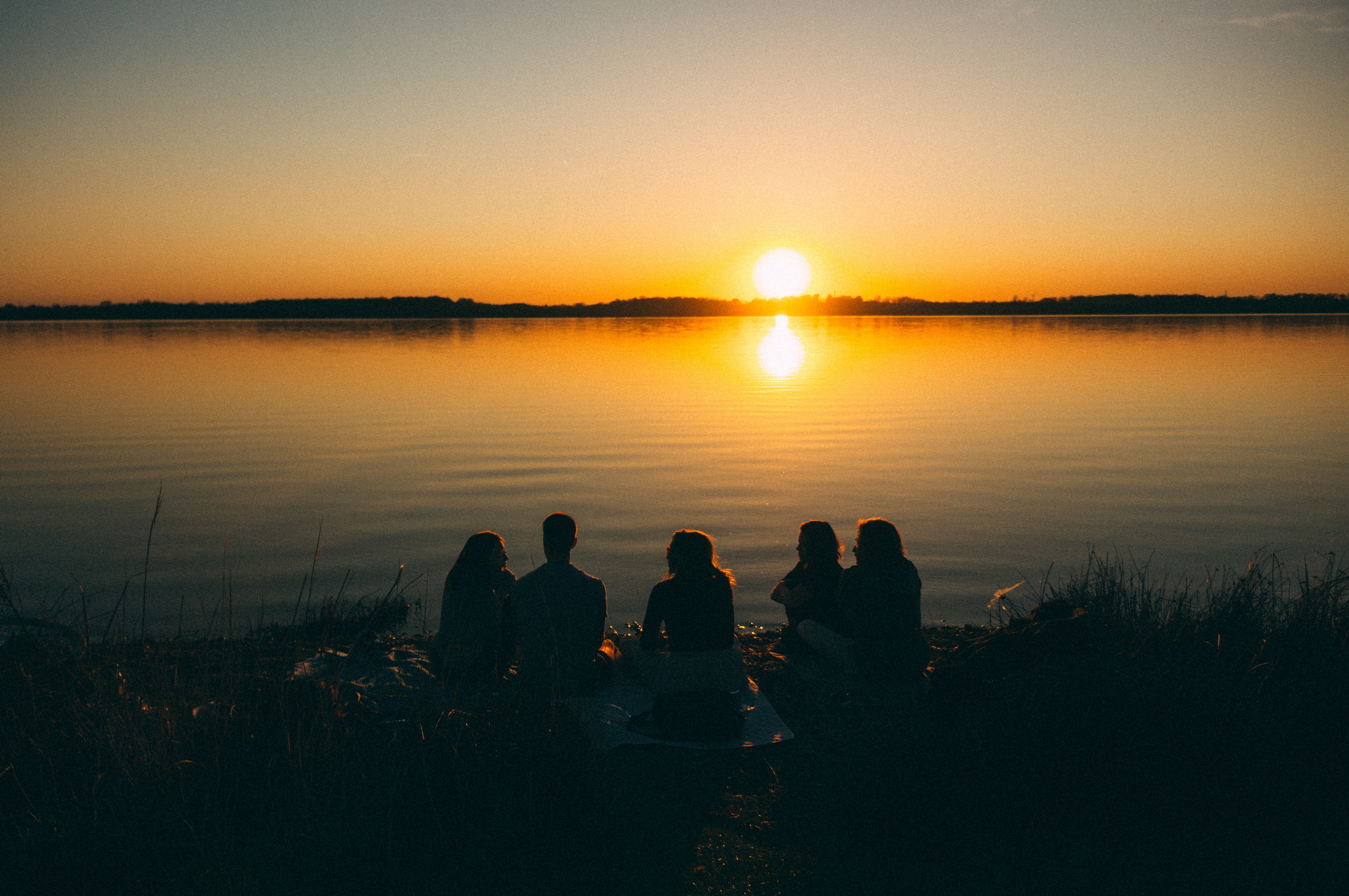 Photo of a sunset over water, with of a group of people gathered on the shore, in silhouette. 