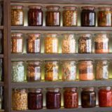 Photo of a shelf with five rows of glass jars, containing foods of different shapes and colors