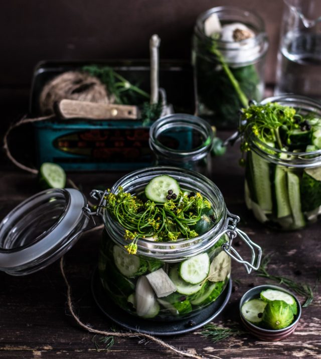 Sliced cucumbers with herbs in a glass jar ready for pickling. 