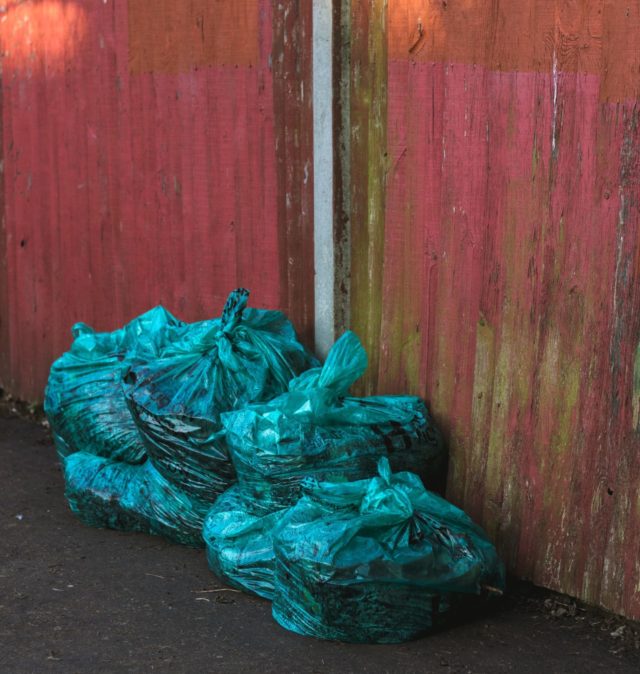 Four bluish garbage bags on the ground next to a red wooden background